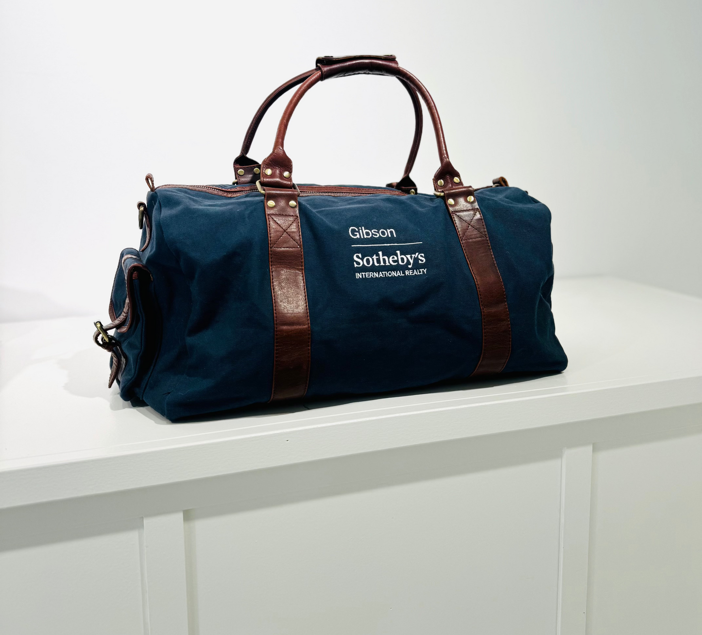 Blue duffel bag with brown leather straps on a white surface